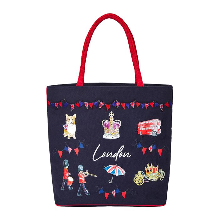 A navy shopping tote bag with contrasting red shoulder straps. The bag features illustrations of London icons including a red London bus, and a corgi dog. 