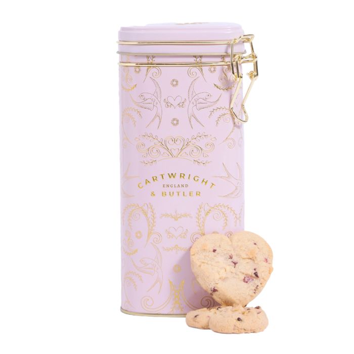 A pink heart-shaped tin with a gold pattern detail, filled with heart-shaped biscuits.