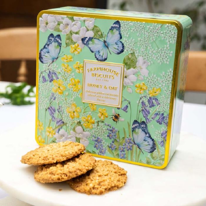 Honey and oat biscuits in a green floral farmhouse tin with butterflies, displayed with teapot and biscuits.