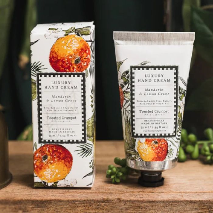 Mandarin and lemon grove luxury hand cream with illustrated citrus packaging displayed on wooden surface with greenery.