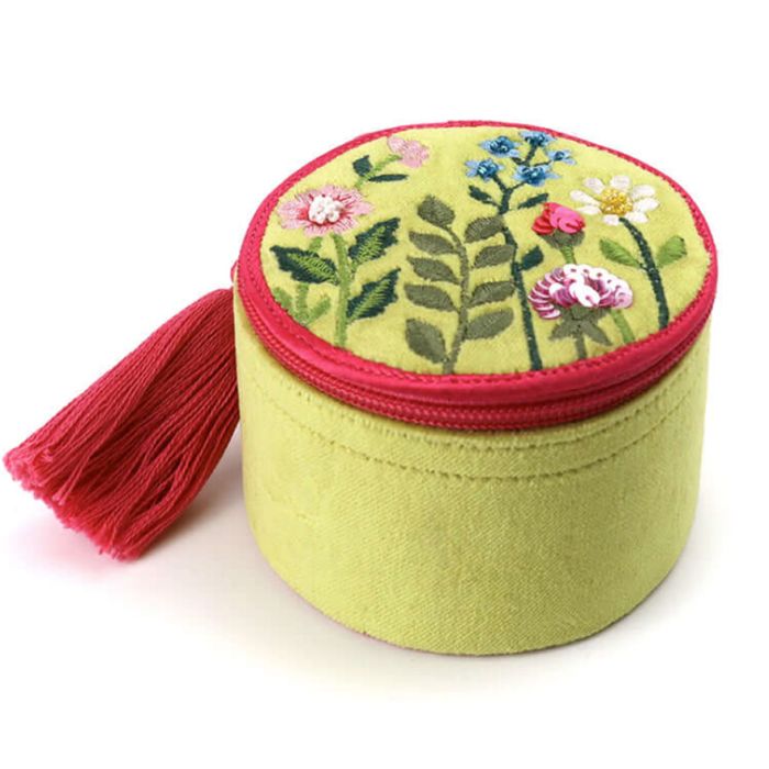 A lime-green circular soft jewellery box with a contrasting pink zip and tassel. The lid is embroidered with flowers and finished with bead and sequin details. 
