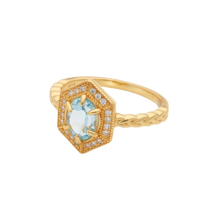 A gold hexagon-shaped ring with an interlaced detail on the band. With a central hand-cut blue topaz stone. 