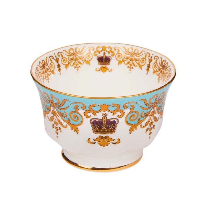A round, white sugar bowl with a small pedestal base with gold rim details and a blue, gold and burgundy pattern including ornate details and a royal crown