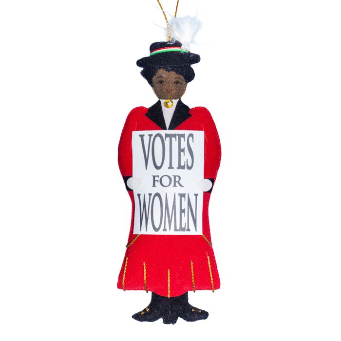 A hanging decoration in the shape of a suffragette wearing a red dress and holding a white votes for women sign. 