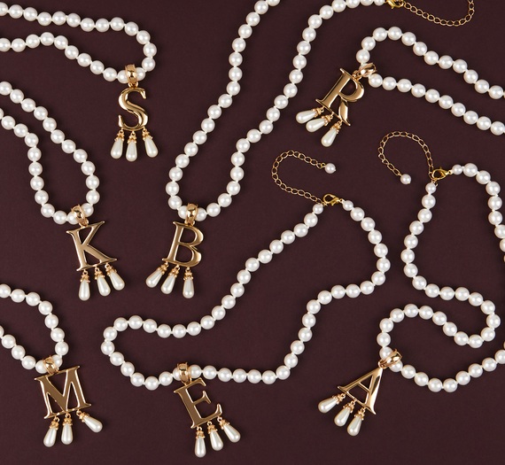A set of gold and pearl initial necklaces in the style of Anne Boleyn's B necklace laid on a burgundy background.