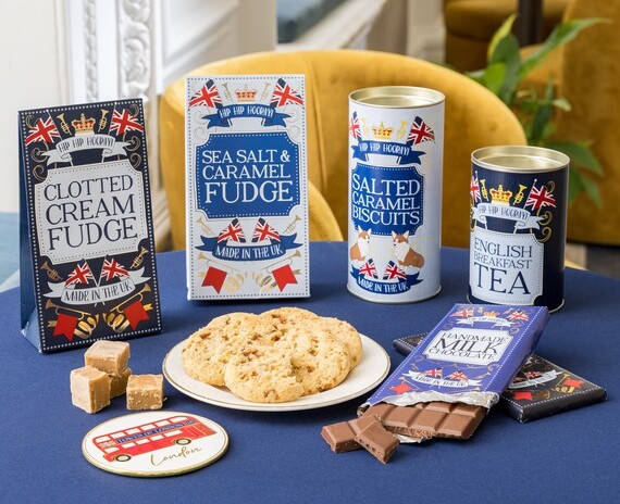 A set of food gifts in blue illustrated packaging on a table with cookies, chocolate and fudge laid out in front.
