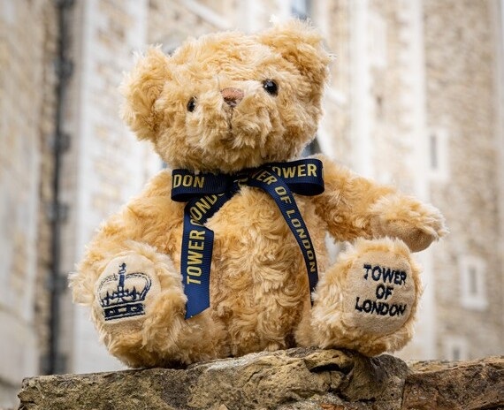 A light-brown teddy bear wearing a navy ribbon sat on a wall at the Tower of London.